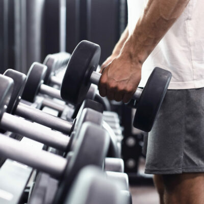 Fitness man in training showing exercises with dumbbells in gym. Fitness man in training showing exercises with dumbbells in gym